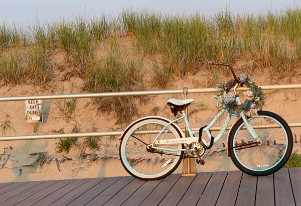 Boardwalk with a bicycle locked to a rail, a sand dune in the background with a sign "keep off dunes"